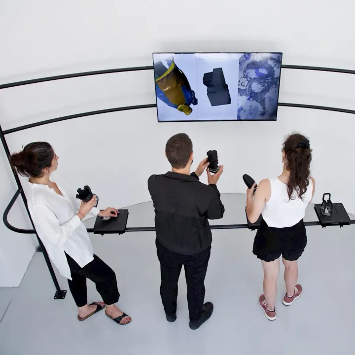 Visitors at MUDAC handling 3D-printed replicas in front of a screen showing the scanned works